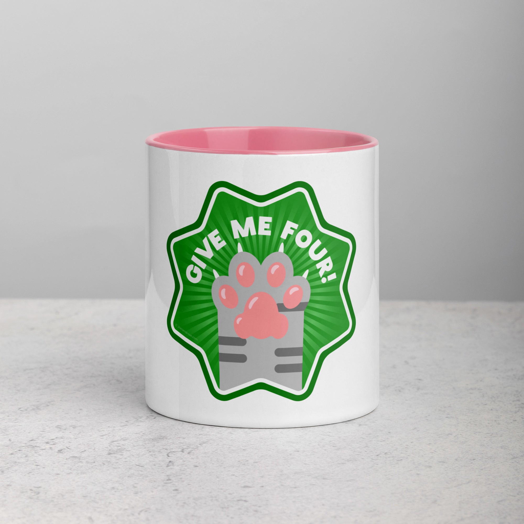 front facing image of a white mug with pink interior and handle. Mug has image of a grey tabby cats paw on a green 8 sided star with the text 'give me four' 